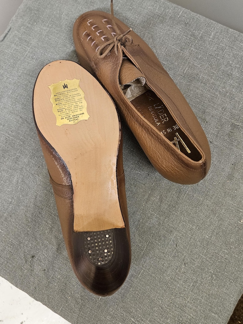 May include: A pair of brown leather shoes with laces. The shoes have a label on the sole that reads "AS HI 30" and "G. LIDER,  TANGUIA".