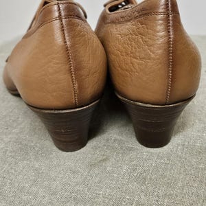 May include: A pair of brown leather heeled shoes with lace-up fronts. The shoes have a slightly pointed toe and a low block heel.