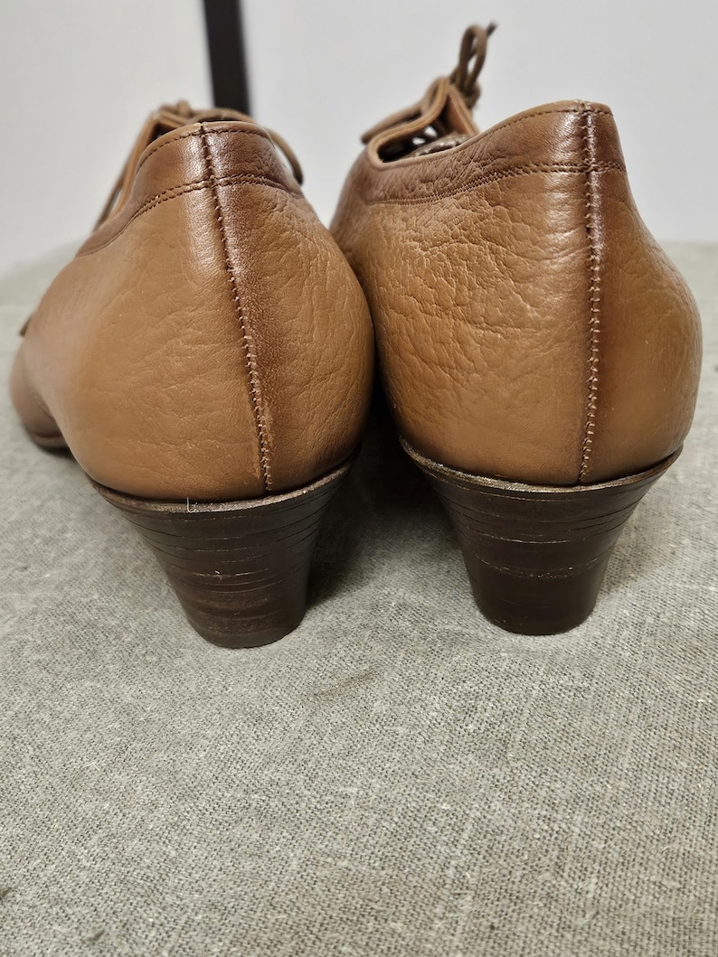May include: A pair of brown leather heeled shoes with lace-up fronts. The shoes have a slightly pointed toe and a low block heel.
