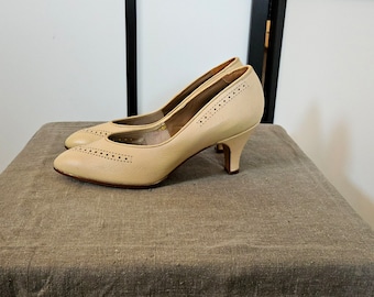 May include: A pair of beige high-heeled shoes with a pointed toe and a decorative perforated pattern.