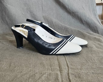 Pode incluir: Um par de sapatos de salto alto branco e preto com uma tira de slingback. Os sapatos têm uma parte superior de couro preto com listras brancas e uma ponta de couro branco.