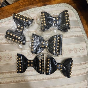 May include: Five black velvet bows with gold studs. The bows are packaged in clear plastic bags.