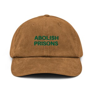 Puede incluir: Una gorra de béisbol de pana marrón con texto bordado en verde que dice "ABOLISH PRISONS".