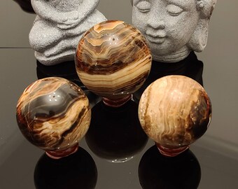 May include: Three brown and white striped spheres, each with a different pattern, are displayed on a black surface. The spheres are made of polished stone and have a smooth, glossy finish.