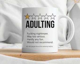 May include: White ceramic mug with the word "ADULTING" in black, with a rating of one gold star and four black stars. The mug has text below that reads "Fucking nightmare. Way too serious. Hardly any fun. Would not recommend."