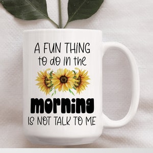 May include: White ceramic mug with a black and white graphic that reads "A fun thing to do in the morning is not talk to me". The graphic is surrounded by three yellow sunflowers.
