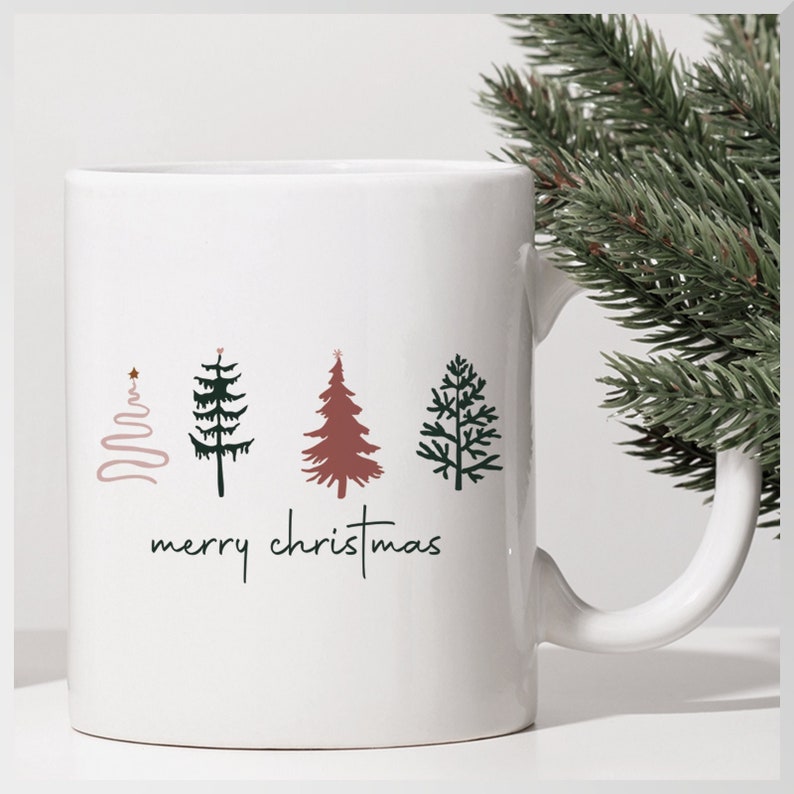 11 oz white ceramic glossy mug that says merry christmas with a graphic of 4 different styles of small Christmas trees.