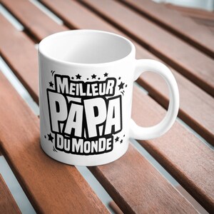 Op de afbeelding: Witte keramische mok met een zwart ontwerp met de tekst "MEILLEUR PAPA DU MONDE", wat "Beste Papa ter Wereld" betekent.