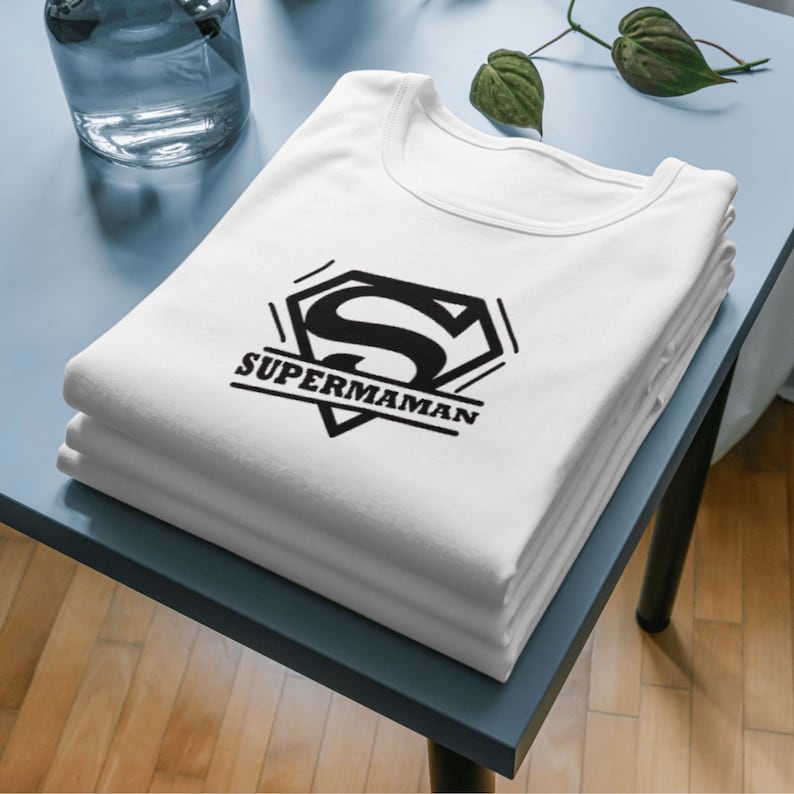 May include: White t-shirt with a black Superman logo and the text "SUPERMAMAN" printed on the front.