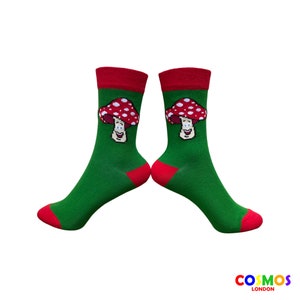 May include: A pair of green socks with red trim and a cartoon mushroom design. The mushroom is red with white spots and has a smiling face.