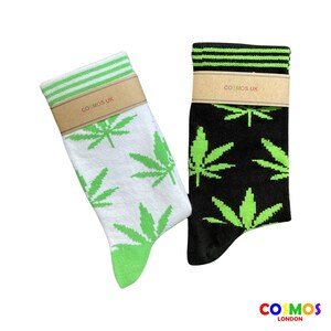 Può includere: Un paio di calzini con un motivo a foglia di marijuana verde. Un calzino è bianco con strisce verdi in alto e l'altro è nero con strisce verdi in alto. Entrambi i calzini hanno il testo "COSMOS UK" sulla confezione.