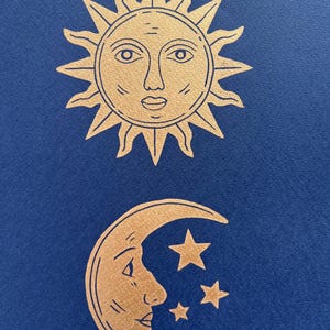 May include: Gold-colored sun and moon illustrations on a dark blue background. The sun has a face with a detailed outline, and the moon features a face with three stars. The celestial theme is prominent.