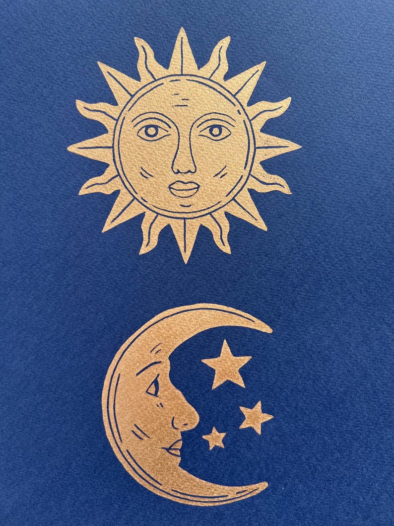 May include: Gold-colored sun and moon illustrations on a dark blue background. The sun has a face with a detailed outline, and the moon features a face with three stars. The celestial theme is prominent.