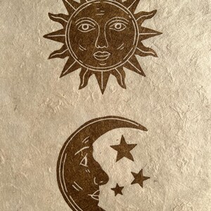 May include: Brown illustration of the sun with a face and radiating lines above a crescent moon with a face and three stars. The celestial bodies are on a textured, off-white background.