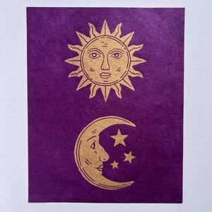 May include: A purple card features a gold sun with a face and a crescent moon with a face and three stars. The sun has spiky rays. The moon and stars are below the sun. The background is a textured purple.