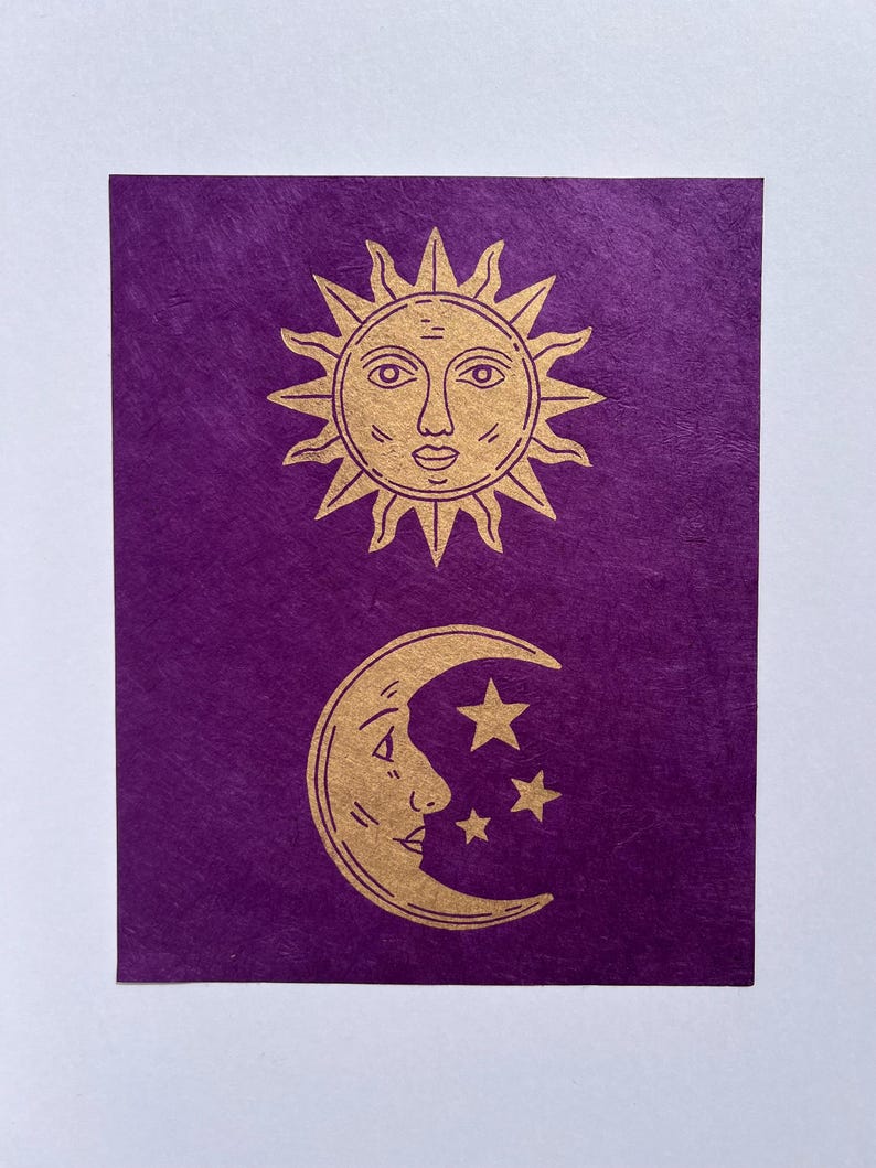 May include: A purple card features a gold sun with a face and a crescent moon with a face and three stars. The sun has spiky rays. The moon and stars are below the sun. The background is a textured purple.