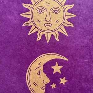 May include: A purple background with gold illustrations of celestial bodies. The top illustration is a sun with a face, and the bottom illustration is a crescent moon with a face and three stars. The design has a mystical theme.