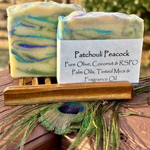 May include: Two bars of handmade soap with a blue, green, and white swirl pattern. The soap is labeled "Patchouli Peacock Pure Olive, Coconut & RSPO Palm Oils, Tinted Mica & Fragrance Oil".