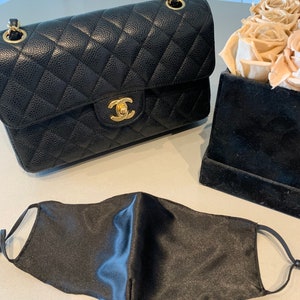 May include: A black quilted leather handbag with a gold chain strap and a gold clasp. A black satin face mask is also pictured.