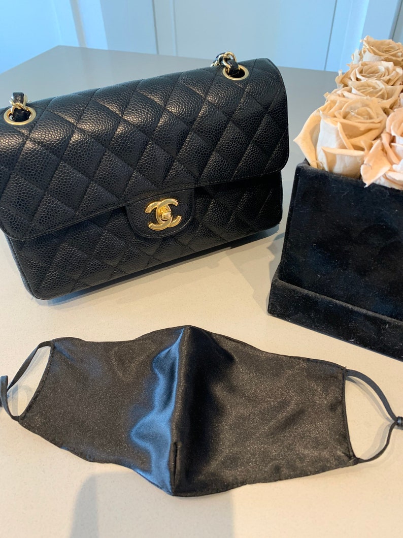 May include: A black quilted leather handbag with a gold chain strap and a gold clasp. A black satin face mask is also pictured.