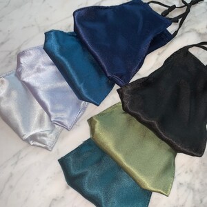 May include: Set of seven satin face masks in various colors, including teal, silver, navy, black, and green. The masks have elastic ear loops.