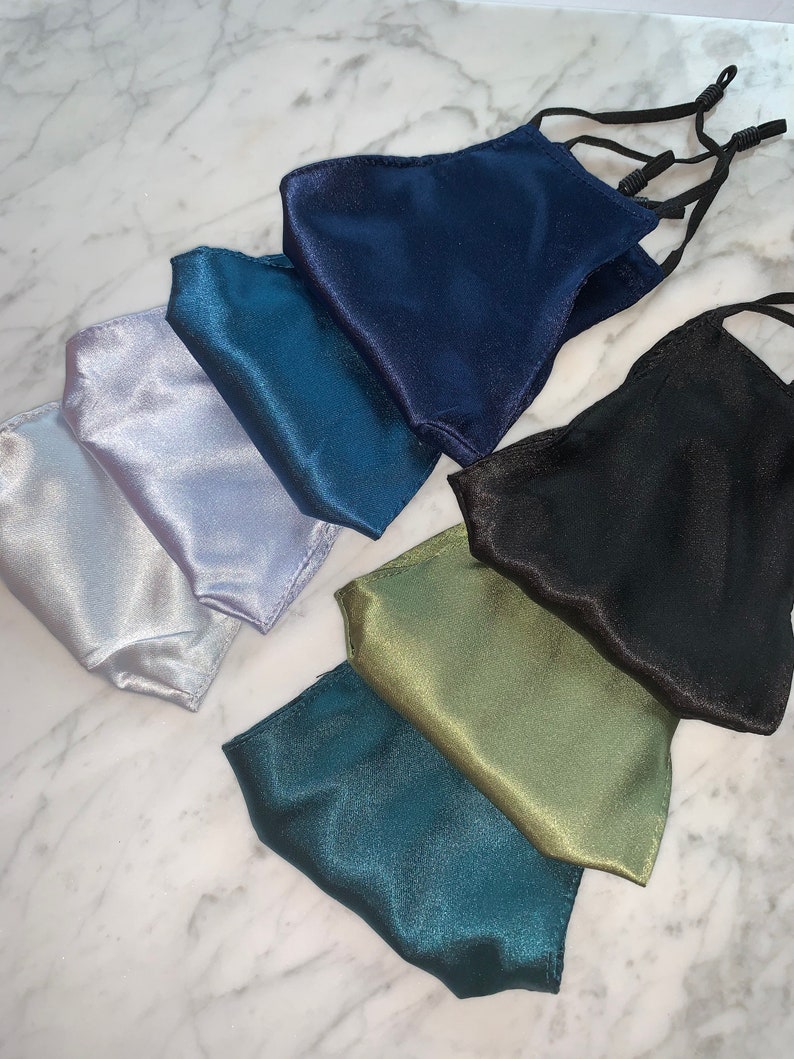 May include: Set of seven satin face masks in various colors, including teal, silver, navy, black, and green. The masks have elastic ear loops.
