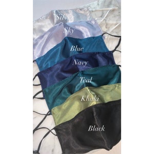 May include: A set of seven satin face masks in various colors, including silver, sky blue, blue, navy, teal, khaki, and black. Each mask has a simple design and is made of a soft, smooth fabric.