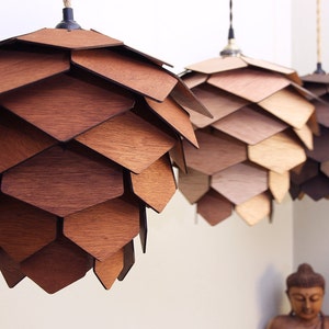 May include: Three wooden pendant lights with a layered, geometric design. The shades are made of various shades of brown wood, creating a warm, natural aesthetic. Each light hangs from a rope cord, adding to the rustic charm. The lights are suspended from the ceiling.