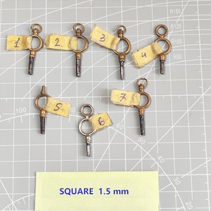 May include: Seven brass-colored metal pocket watch winding keys, each featuring a circular bow and a square-shaped tip. Each key is labeled with a small piece of yellow tape numbered one through seven. A yellow label below reads SQUARE 1.5 mm.