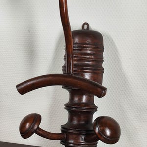 May include: A dark brown, antique wooden coat rack with a mushroom-shaped top, curved arm, and two rounded hooks. The rack has a decorative, turned design and is mounted on a wall.