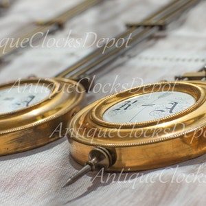 Puede incluir: Cuatro péndulos de reloj antiguos con carcasas de latón y caras blancas. Las caras del reloj tienen números romanos negros y manecillas negras.