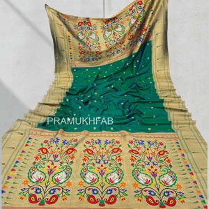 May include: A green and gold saree with intricate floral and paisley embroidery. The saree features a vibrant design with red, blue, yellow, and white accents. The text "PRAMUKHFAB" is visible on the saree.