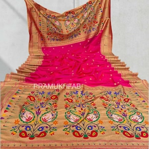 May include: A vibrant pink saree with intricate gold floral and paisley patterns. The saree features a detailed border and a decorative pallu. The text "PRAMUKHFAB" is visible on the saree.
