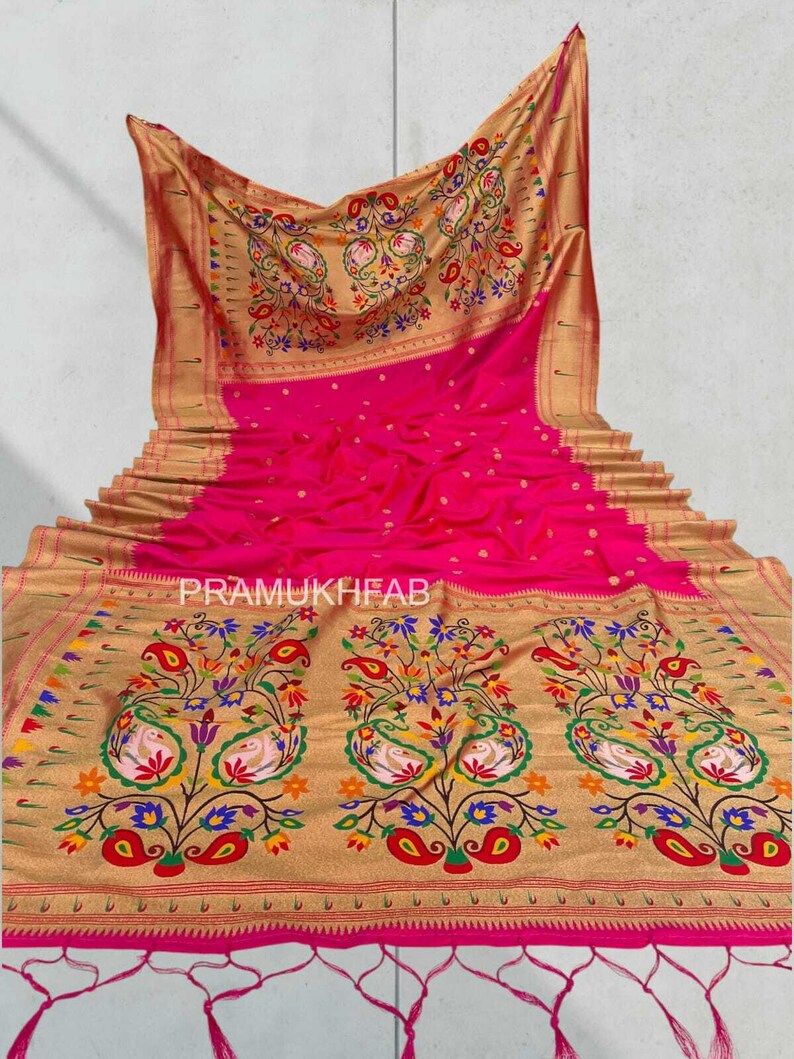 May include: A vibrant pink saree with intricate gold floral and paisley patterns. The saree features a detailed border and a decorative pallu. The text "PRAMUKHFAB" is visible on the saree.