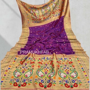 May include: A luxurious purple saree with a gold border and intricate floral and paisley embroidery. The saree features the text "PRAMUKHFAB" and is adorned with colorful accents, creating a vibrant and elegant design.
