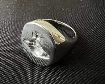 Peut inclure: Une bague signet en argent avec un motif d'orbe en relief. La bague est en métal et a une finition lisse et polie.