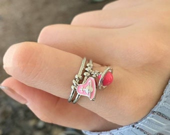 Op de afbeelding: Een set van drie zilveren ringen met roze emaille. De ringen hebben een kleine bolvormige hanger en een grotere hanger met een roze en een witte bolvormige vorm.