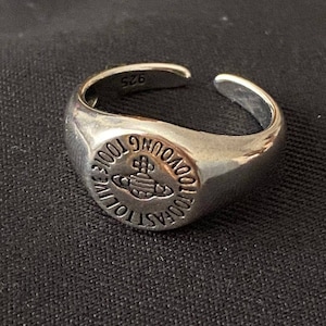May include: A silver signet ring with a raised orb design and the text "Vivienne Westwood" around the orb. The ring is size 52.