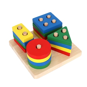 May include: A wooden shape sorter toy with a light wood base. The toy features a yellow rectangle, a blue square, a green triangle, and a red circle, each with wooden pegs. The shapes are stacked on top of each other in layers of different colors.
