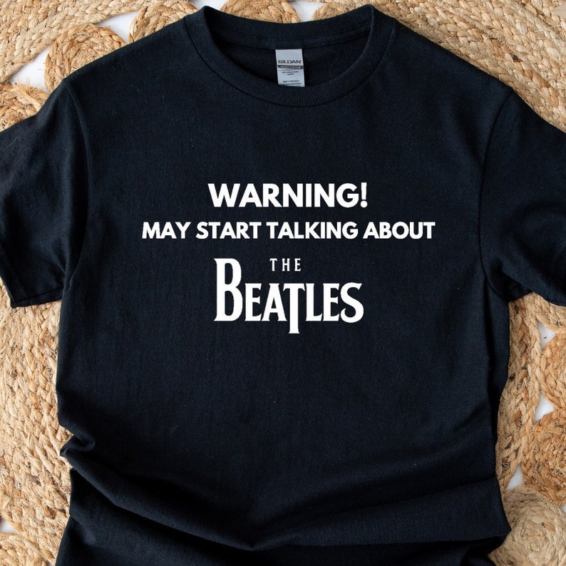 May include: Black t-shirt with white text that reads "WARNING! MAY START TALKING ABOUT THE BEATLES".