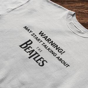 May include: A gray t-shirt with black text that reads "WARNING! MAY START TALKING ABOUT THE BEATLES".
