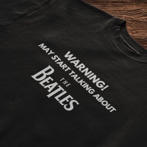 May include: Black t-shirt with white text that reads "WARNING! MAY START TALKING ABOUT THE BEATLES".