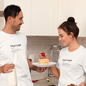 May include: A couple wearing white t-shirts with the word "Marriage" and its definition printed on them. The man is holding a glass of milk and the woman is holding a plate of pancakes with a strawberry on top.