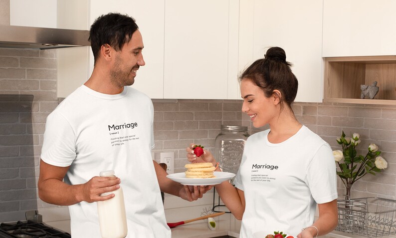 May include: A couple wearing white t-shirts with the word "Marriage" and its definition printed on them. The man is holding a glass of milk and the woman is holding a plate of pancakes with a strawberry on top.