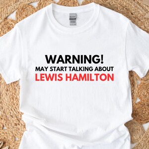 May include: White t-shirt with black text that reads "WARNING! MAY START TALKING ABOUT LEWIS HAMILTON".