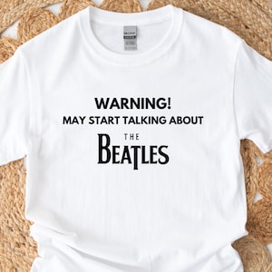 May include: White t-shirt with black text that reads "WARNING! MAY START TALKING ABOUT THE BEATLES".