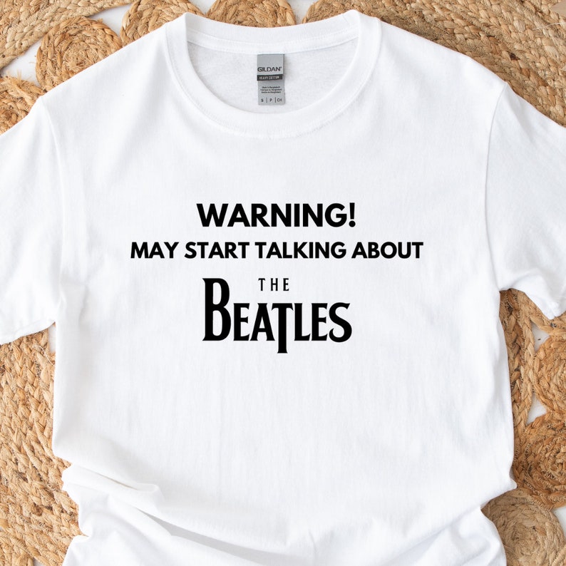 May include: White t-shirt with black text that reads "WARNING! MAY START TALKING ABOUT THE BEATLES".