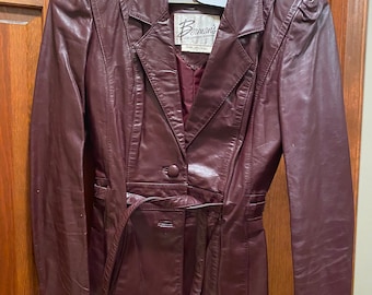 May include: A burgundy leather jacket with a belt and a single button closure. The jacket has a label that reads "Bermans The Leather Experts".