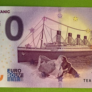 Può includere: Un biglietto da banca souvenir viola e blu con la nave RMS Titanic. Il biglietto da banca ha uno zero grande stampato su di esso e il testo "RMS TITANIC" e "EURO SOUVENIR".