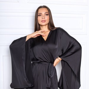 May include: A black satin robe with long, wide sleeves and a wrap closure. The robe has a V-neckline and a sash tie at the waist.
